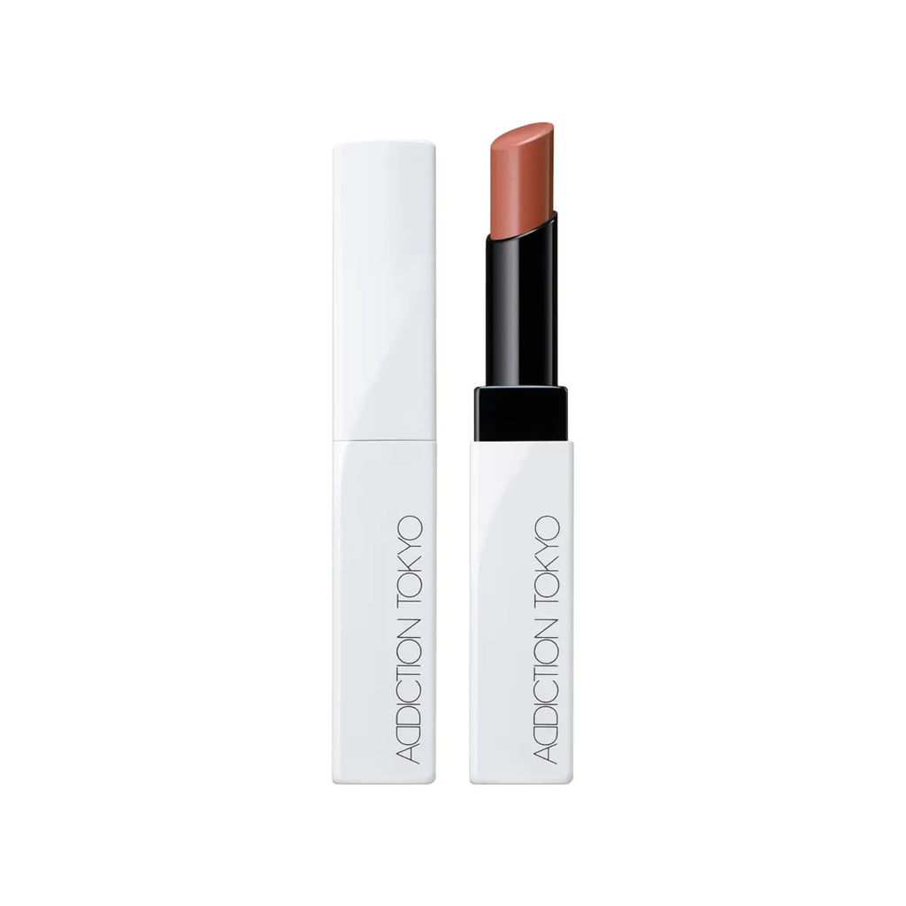 Addiction Tokyo Lip Balm Glow Tint in a warm peach shade, offering a moisturizing formula in a stylish white and black tube.