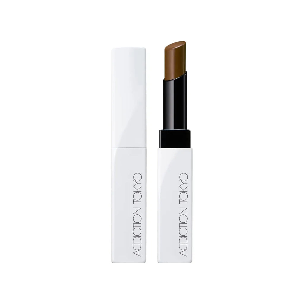 Addiction Tokyo Lip Balm Glow Tint in a warm brown shade, designed in a chic white and black tube for a bold glossy look.