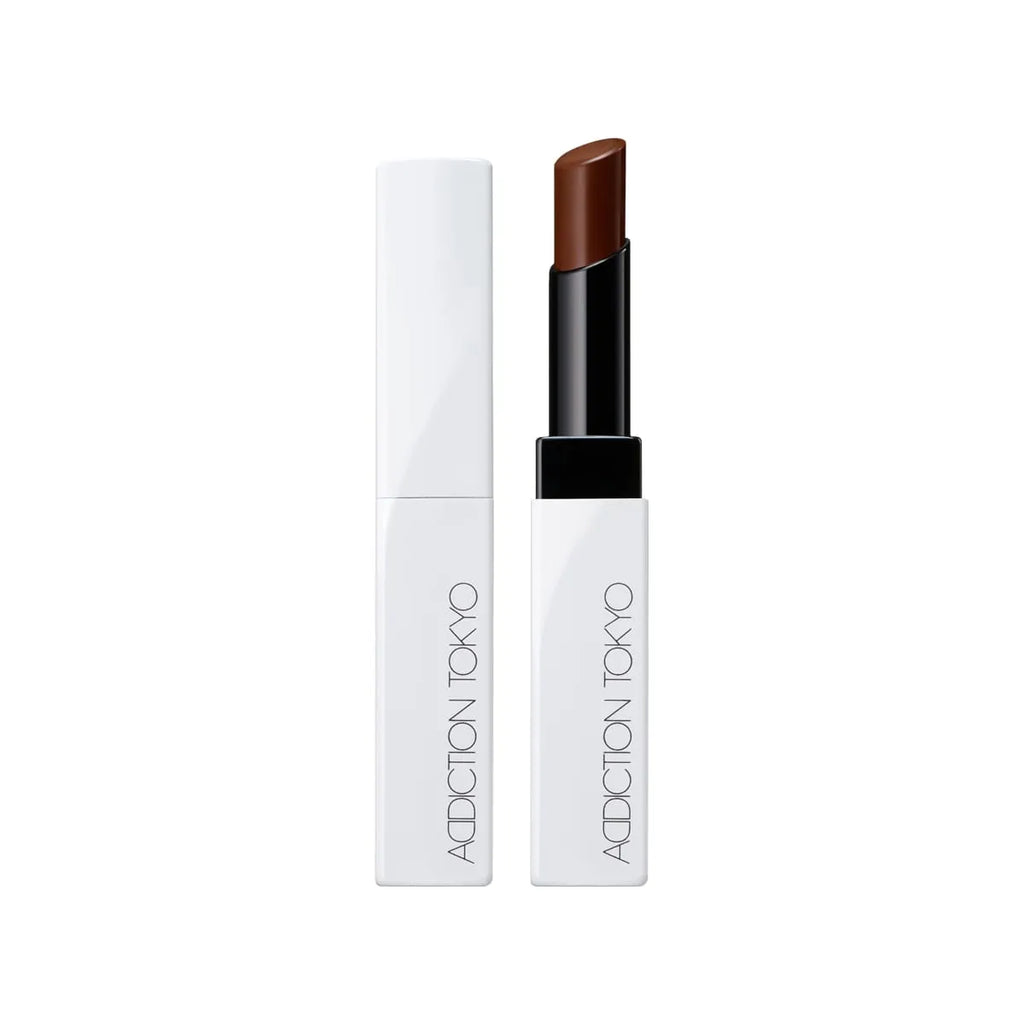 Addiction Tokyo Lip Balm Glow Tint in a rich burgundy shade, presented in a minimalist white and black tube for a luxurious glossy finish.