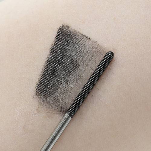 Canmake Metal Look Mascara swatch in black on skin, with the wand displaying its fine bristles for smooth application.