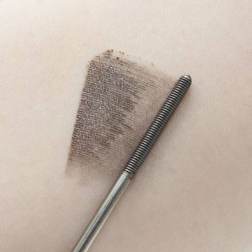 Canmake Metal Look Mascara swatch in brown on skin, with the wand highlighting its precision bristles for smooth application.