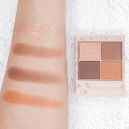 Swatches of Canmake Silky Flare Eyes matte type palette on an arm, showcasing four neutral shades alongside the palette for comparison.