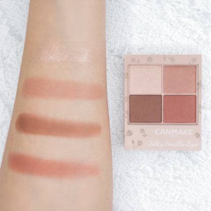 Swatches of Canmake Silky Flare Eyes matte type palette on an arm, displaying peach and brown shades alongside the palette for reference.