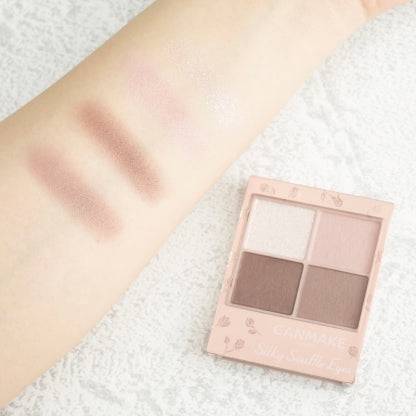 Swatches of Canmake Silky Flare Eyes matte type palette on an arm, displaying pastel pink and mauve shades alongside the palette.