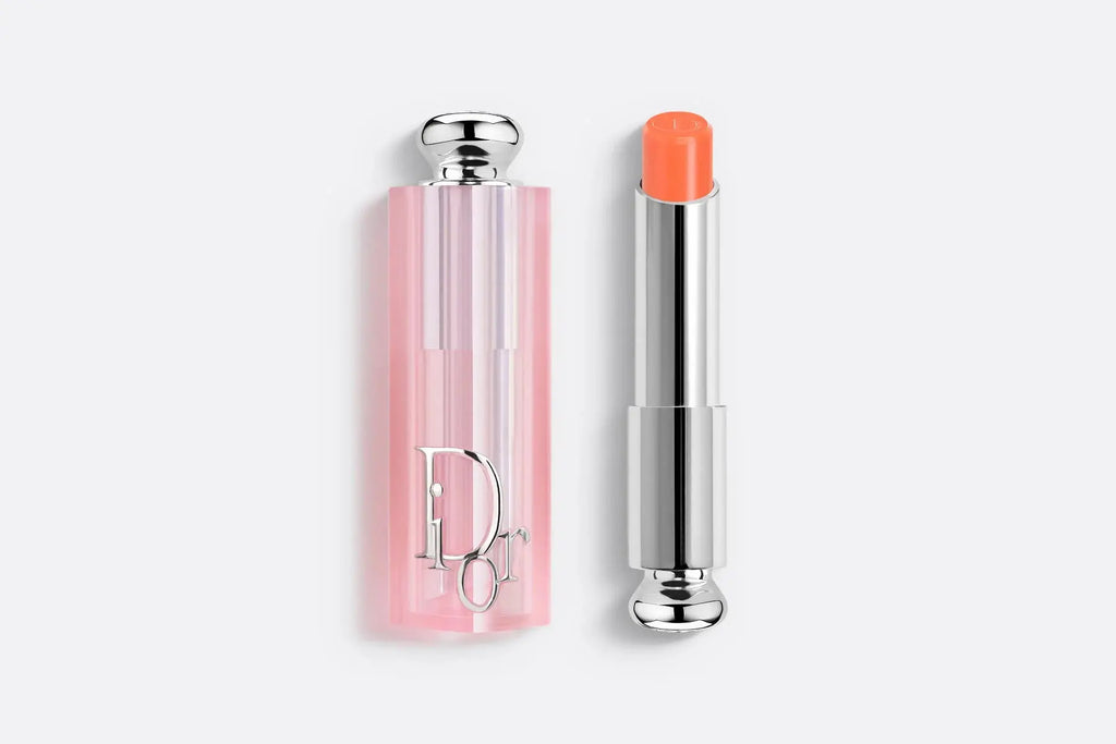 Dior Addict Lip Glow lipstick in a soft coral hue, enhancing lips with a sheer, moisturizing formula. Packaged in a pink translucent case.