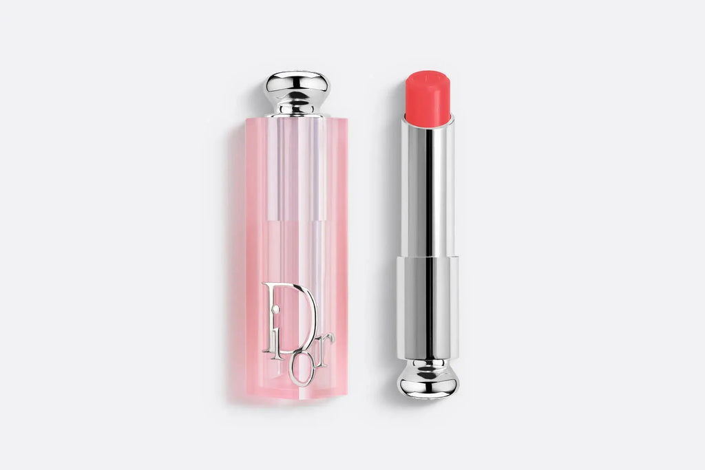 Dior Addict Lip Glow lipstick in a bright coral shade, delivering hydration and a natural glow. Packaged in a pink translucent tube.