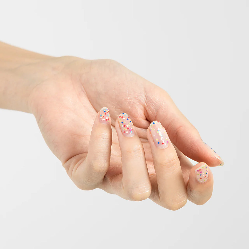 Hand with nails painted in multicolor confetti glitter Elégance Lacquer, showcasing a fun and vibrant finish for celebrations.