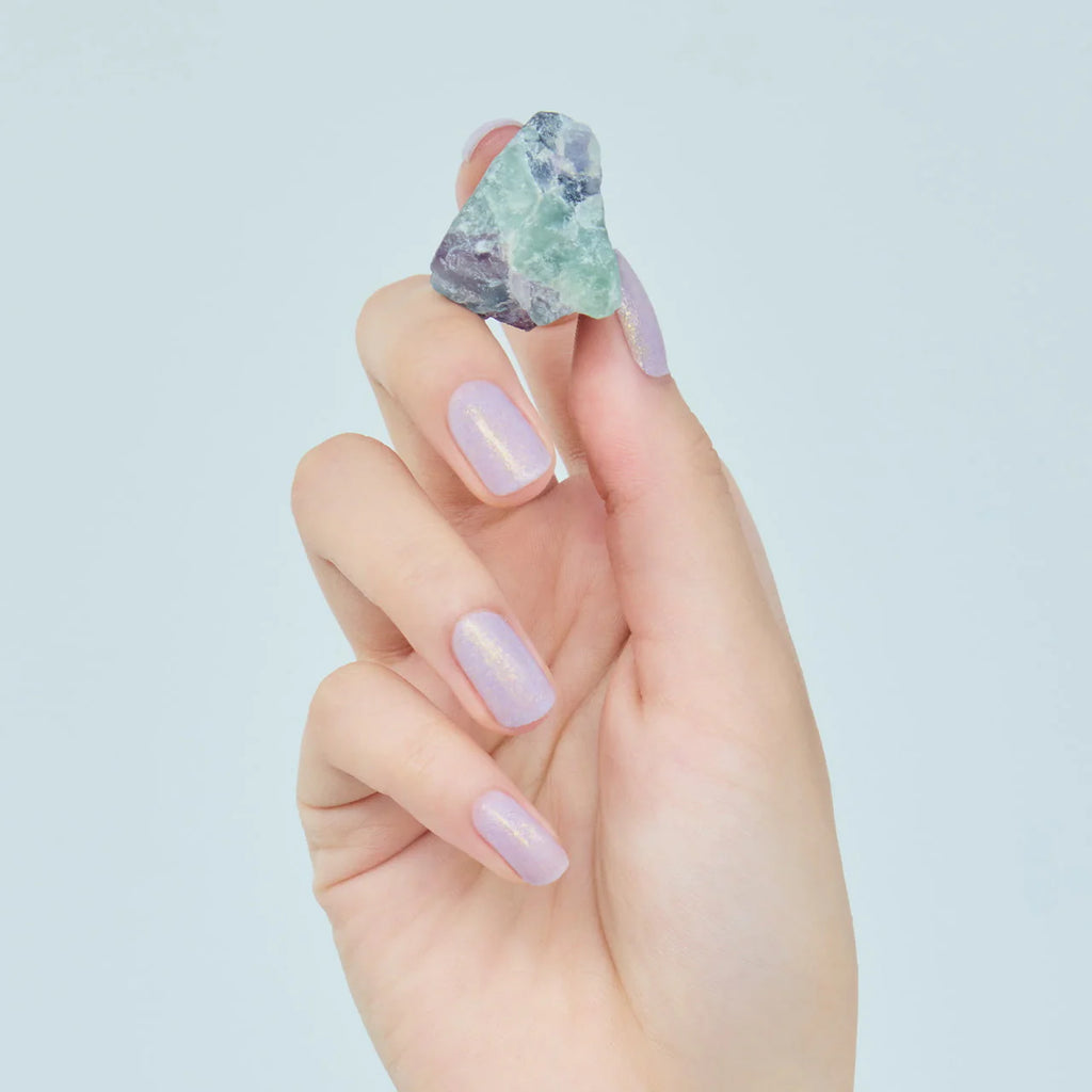 Hand with nails painted in lavender Elégance Lacquer, holding a gemstone, showcasing a soft shimmer finish for a refined look.