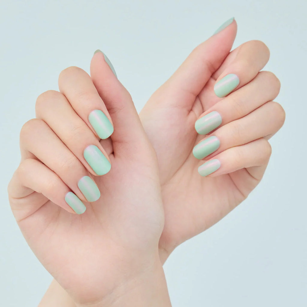 Hands with nails painted in mint green Elégance Lacquer, showcasing a soft shimmer finish for a chic and trendy look.