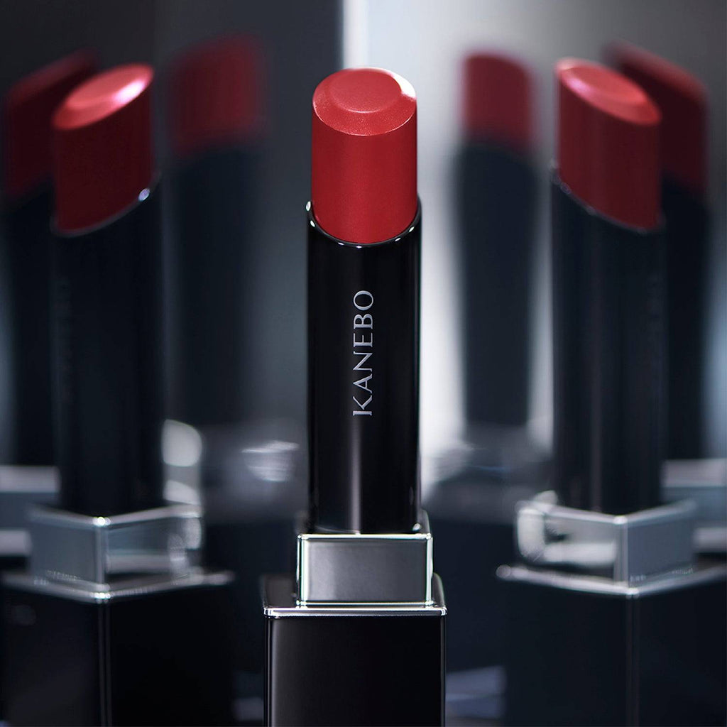 Kanebo Rouge Star Vibrant lipstick in a brownish-red tone, displayed with reflective surfaces for a luxurious look.