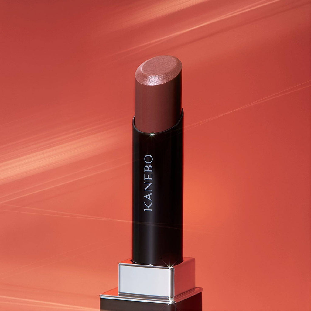 Kanebo Rouge Star Vibrant lipstick in a nude brown tone, set against a glowing background with a smooth, radiant finish.