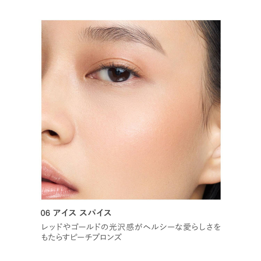 Close-up of RMK Radiant Color Stick 6.4g in shade 06 Ice Spice applied on skin, showcasing a warm peach bronze shimmer.