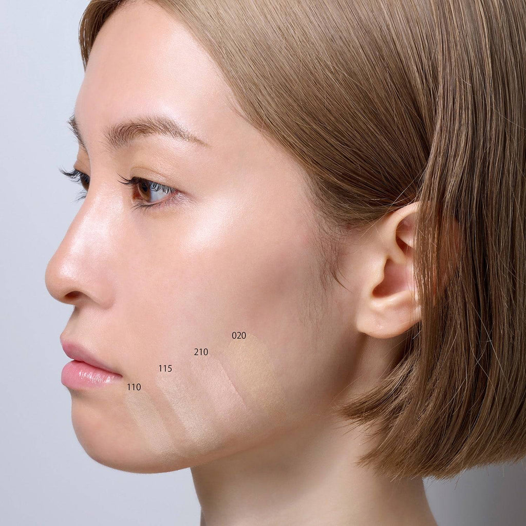 Model showcasing Suqqu The Foundation 30g with shade swatches 110, 115, 210, and 020 applied on the jawline for comparison. Cream makeup with a rich glossy glow finish.