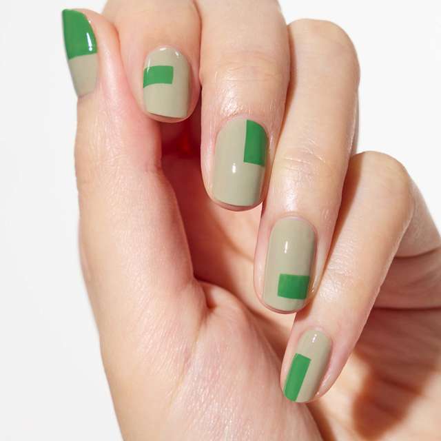 Hand with nail art featuring Three Nail Lacquer in olive green and vibrant green shades, showcasing a geometric design.