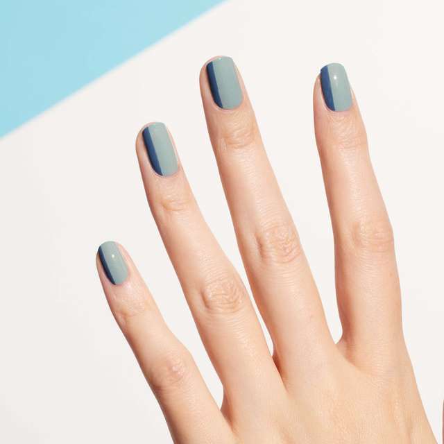 Hand with nail art featuring Three Nail Lacquer in teal and gray shades, creating a chic and contemporary design.