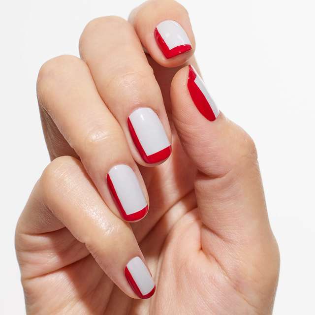 Hand with nail art featuring Three Nail Lacquer in white and red shades, showcasing a bold and graphic manicure.