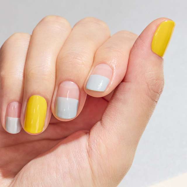 Hand with nail art featuring Three Nail Lacquer in yellow and light gray shades, showcasing a modern and stylish manicure.